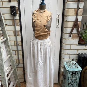 Può includere: Manichino da sarta antico con busto beige e gonna bianca. Il manichino ha una base blu e un terminale blu. Il busto è ricoperto di tessuto strappato. La gonna è lunga e arricciata in vita.