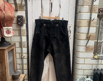 Puede incluir: Pantalón de pana negro de cintura alta y cierre de botón. El pantalón tiene dos bolsillos grandes en la parte delantera y un solo botón a cada lado de la cintura.