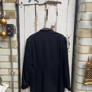 May include: A black blazer with a velvet collar. The blazer is hanging on a white door with a number "21" on it.