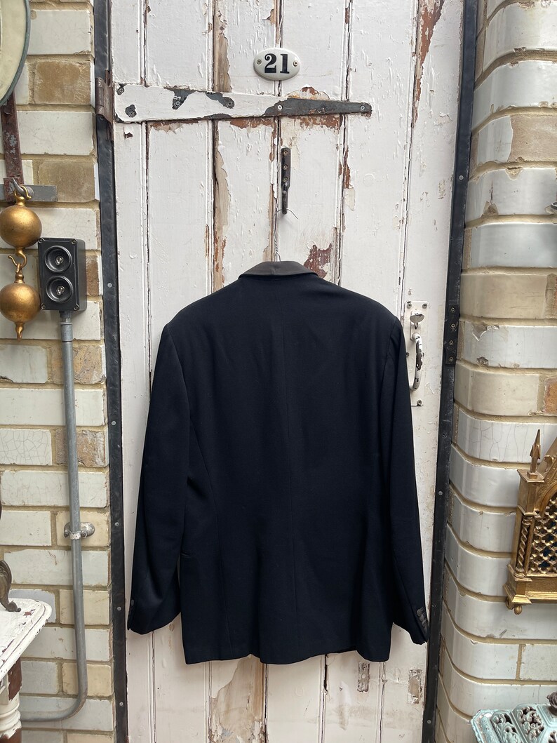 May include: A black blazer with a velvet collar. The blazer is hanging on a white door with a number "21" on it.