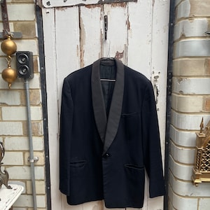 May include: A black tuxedo jacket with a satin shawl collar. The jacket is hanging on a hook against a white wooden door.