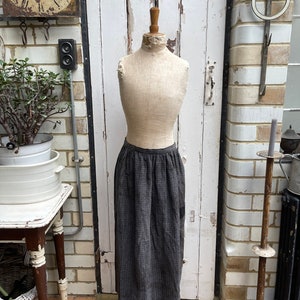 May include: A grey and black checked skirt on a vintage dress form. The skirt is long and flowing, with a gathered waist.