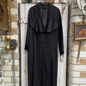May include: A long black coat with a ruffled collar and a single button closure.