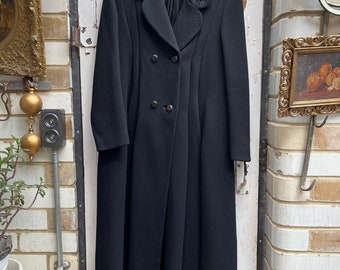 Può includere: Un lungo cappotto di lana nera con chiusura a doppio petto e collo alto. Il collo presenta un design ricamato decorativo.