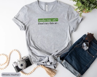Peut inclure: T-shirt gris avec une boîte verte qui dit "sudo rm -rf*" et le texte "Don't try this at~" en noir.
