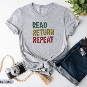 May include: A gray t-shirt with the text "READ RETURN REPEAT" in a vintage style font. The text is in green, yellow, and red.