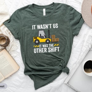 May include: A green t-shirt with the text "It wasn't us. It was the other shift." and a cartoon image of a yellow forklift with boxes on it.