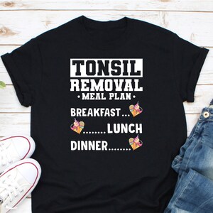 May include: Black t-shirt with white text that reads "Tonsil Removal Meal Plan" with ice cream cones and hearts as a graphic.
