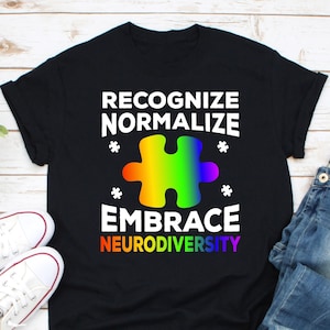 May include: Black t-shirt with white text that reads "Recognize Normalize Embrace Neurodiversity". A rainbow coloured puzzle piece is in the centre of the text.