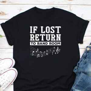 May include: Black t-shirt with white text that reads "IF LOST RETURN TO BAND ROOM" and musical notes.