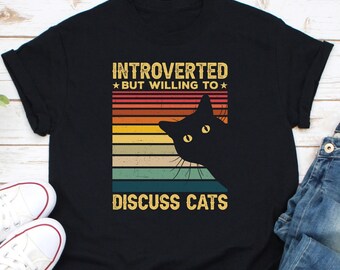 May include: Black t-shirt with a vintage-style graphic of a black cat peeking over a rainbow stripe design. The text "Introverted *But Willing To* Discuss Cats" is printed on the shirt.