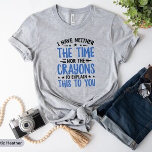 May include: A heather grey t-shirt with the text "I have neither the time nor the crayons to explain this to you" printed in black and blue.