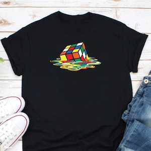May include: A black t-shirt with a colorful graphic of a melting Rubik's cube. The cube is red, orange, yellow, green, blue, and white. The melting effect is in shades of yellow, green, blue, and orange.