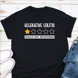 May include: Black t-shirt with white text that reads "Ulcerative Colitis" and a one-star rating with the text "Would Not Recommend".