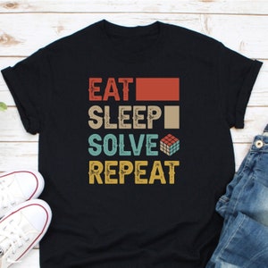 May include: Black t-shirt with a vintage-style graphic that reads "Eat Sleep Solve Repeat" with a Rubik's Cube icon.
