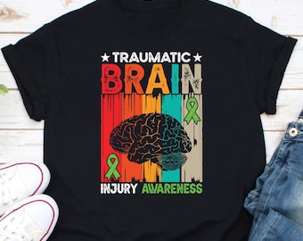 May include: A black t-shirt with a vintage-style graphic design featuring a brain with a green ribbon and the text "Traumatic Brain Injury Awareness".