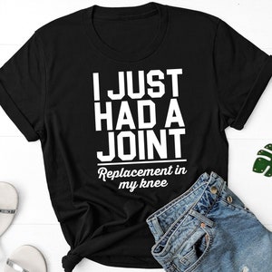 May include: Black t-shirt with white text that reads "I just had a joint replacement in my knee".