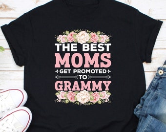 以下が含まれることがあります： ピンクの文字で「The Best Moms Get Promoted To Grammy」と書かれた黒いTシャツ。テキストの周りにピンクの花が咲いています。