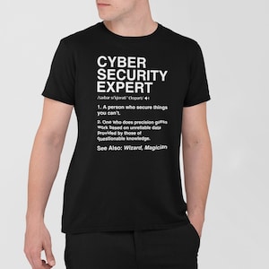 May include: A black t-shirt with a white graphic that defines a "Cyber Security Expert" as a person who secures things you can't and someone who makes educated guesses based on unreliable data. The graphic also includes the text "See Also: Wizard, Magician".