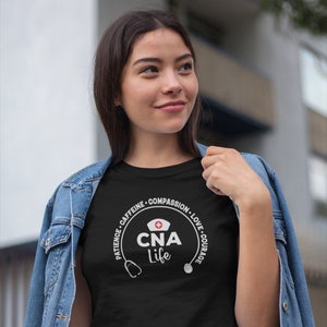 May include: Black t-shirt with a white circle graphic that says "CNA life" with a stethoscope on each side. The circle graphic also has the words "Patience, Caffeine, Compassion, Love, Courage" around it.