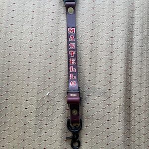 May include: A brown leather key chain with a black clip and a red embroidered name "MASTELLO" on it.