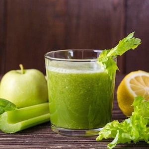 May include: A glass of green smoothie with celery, apple, and lemon on a wooden surface.