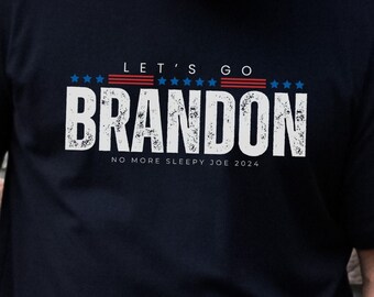 May include: Black t-shirt with a white distressed graphic that says "Let's Go Brandon" with red, white, and blue stars and stripes. The text "No More Sleepy Joe 2024" is below the graphic.