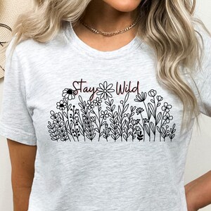 May include: A gray t-shirt with a black and white floral design and the text "Stay Wild" in maroon.