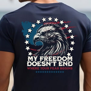 May include: A navy blue t-shirt with a graphic of an eagle's head with a red, white, and blue American flag design. The text "MY FREEDOM DOESN'T END WHERE YOUR FEAR BEGINS" is printed on the shirt.