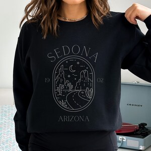 May include: Black sweatshirt with a white graphic design of a desert landscape with the text "SEDONA 1902 ARIZONA".