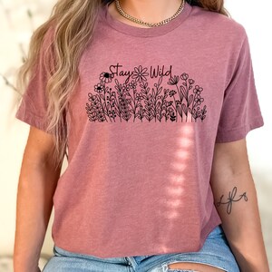 May include: A mauve cropped t-shirt with a black graphic of flowers and the text "Stay Wild".