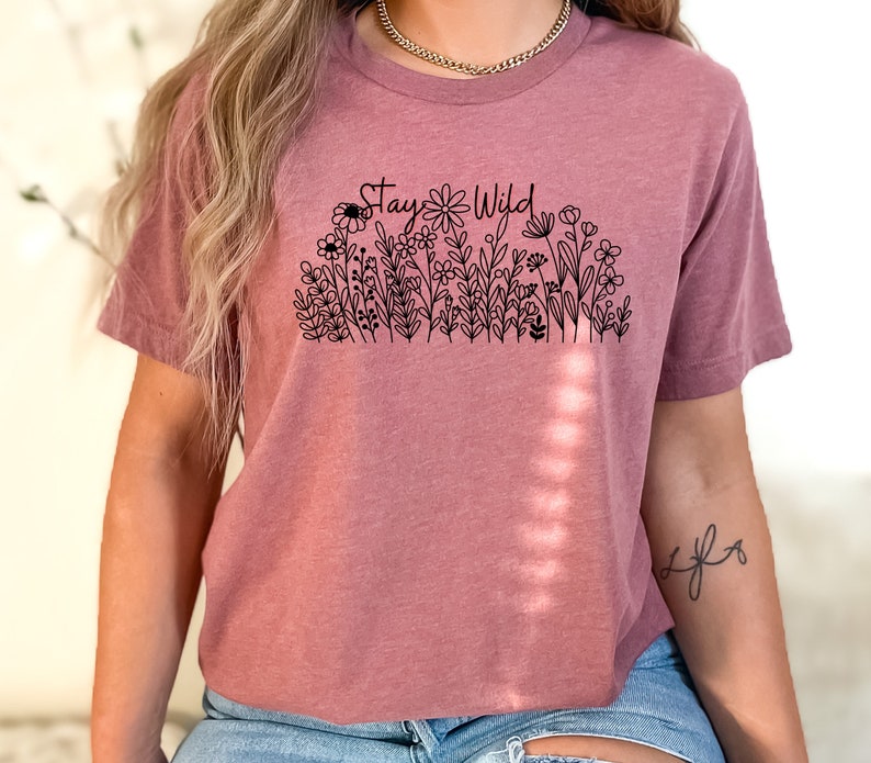 May include: A mauve cropped t-shirt with a black graphic of flowers and the text "Stay Wild".