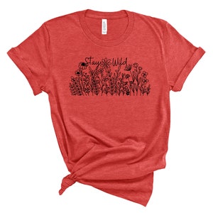 May include: Red t-shirt with a black graphic that says "Stay Wild" and features a line of flowers and a bee.