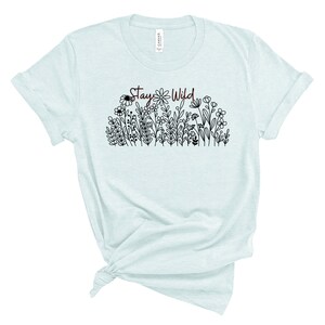 May include: A light blue t-shirt with a black and white floral design and the text "Stay Wild" in maroon.