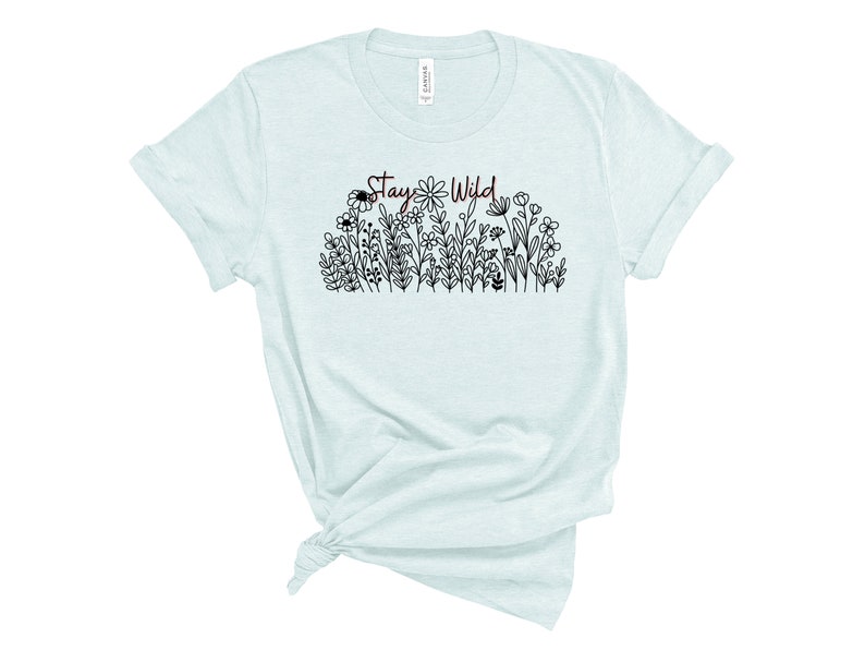 May include: A light blue t-shirt with a black and white floral design and the text "Stay Wild" in maroon.
