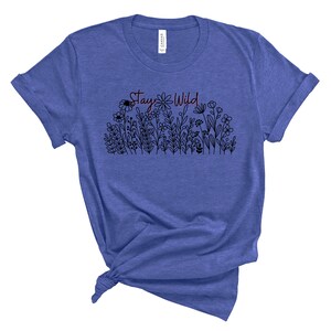 May include: A blue t-shirt with a black and white floral design and the text "Stay Wild" in red.