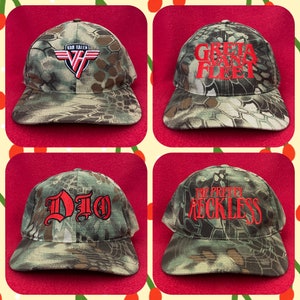 May include: Four camouflage baseball caps with different band logos. The logos are Van Halen, Greta Van Fleet, Dio, and The Pretty Reckless. The caps are all in a camouflage pattern.