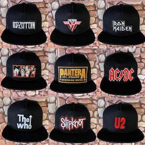 May include: Nine black trucker hats with various band logos. The logos include "Led Zeppelin," "Van Halen," "Iron Maiden," "Kiss," "Pantera," "AC/DC," "The Who," "Slipknot," and "U2." Each hat has a black brim and mesh back.