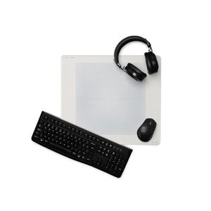 Puede incluir: Un teclado de ordenador negro, un ratón inalámbrico negro y unos auriculares negros dispuestos sobre una alfombrilla de escritorio rectangular blanca con un sutil patrón de cuadrícula gris claro. El teclado está en ángulo, mientras que el ratón y los auriculares descansan sobre la alfombrilla.