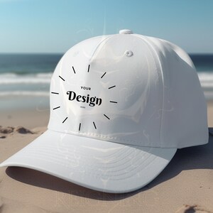 May include: White baseball cap with a black circle and the text "YOUR Design HERE" on the front. The cap is lying on a sandy beach.