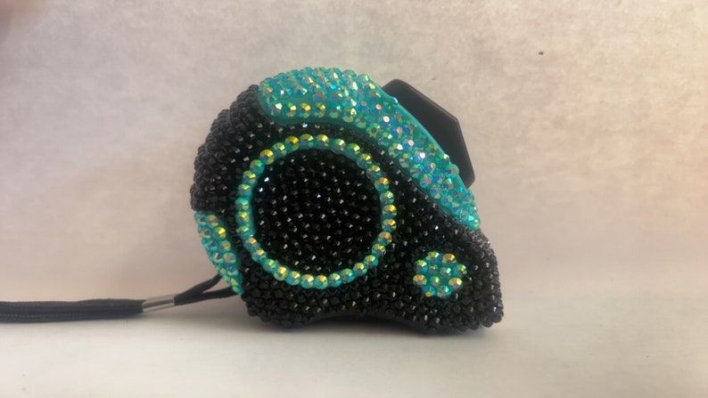 May include: A black and teal measuring tape with rhinestones covering the entire surface.