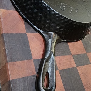 May include: Black cast iron skillet with a hammered finish and a loop handle. The skillet has the number "87" stamped on the bottom.
