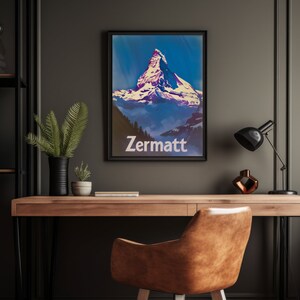 Puede incluir: Un p&oacute;ster enmarcado con una est&eacute;tica vintage que presenta un pico de monta&ntilde;a con nieve en la cima. La monta&ntilde;a se encuentra sobre un cielo azul con nubes. El texto "Zermatt" est&aacute; impreso en blanco en la parte inferior del p&oacute;ster.