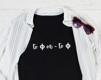 May include: A black V-neck t-shirt with the white text "to Φ or ~ to Φ" printed on the front, layered under a white and black striped button-down shirt, paired with blue denim jeans, red canvas sneakers, and dark-tinted sunglasses.