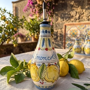 May include: A ceramic cruet with a tapered neck and a metal pour spout, featuring hand-painted yellow lemons, green leaves, and blue accents. The word limoncello is written in blue script on the front, surrounded by decorative patterns.