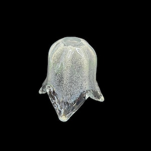 May include: A clear, bell-shaped glass object with a speckled, iridescent finish. The glass has a flared, scalloped edge and a rounded top. The object is set against a black background, highlighting its form and texture.