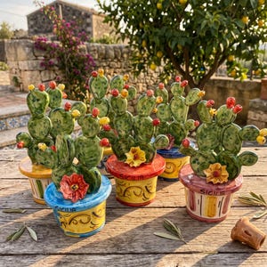 Peut inclure: Une collection de quatre sculptures en céramique représentant des figuiers de Barbarie dans des pots peints à la main. Chaque cactus présente des raquettes vertes avec des fruits rouges et jaunes et une fleur en céramique. Les pots portent le mot SICILIA.