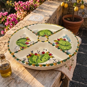 Puede incluir: Un plato de servicio redondo de cerámica color crema dividido en cuatro secciones. Cada sección presenta una ilustración de cactus verde pintada a mano con frutos rojos pequeños. El borde tiene un patrón amarillo y verde.