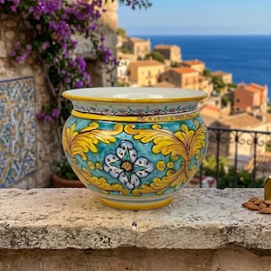 Pode incluir: Um vaso de cerâmica redondo com um fundo turquesa vibrante, motivos de folhas de acanto amarelas pintadas à mão e um design floral azul central. A borda é decorada com um padrão repetitivo e o texto DEC. A MAND S. STEF CPH.