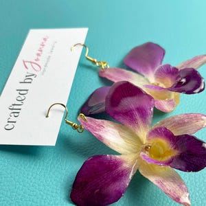 May include: Purple and white orchid flower earrings with gold hooks. The earrings are handmade and feature real pressed flowers.